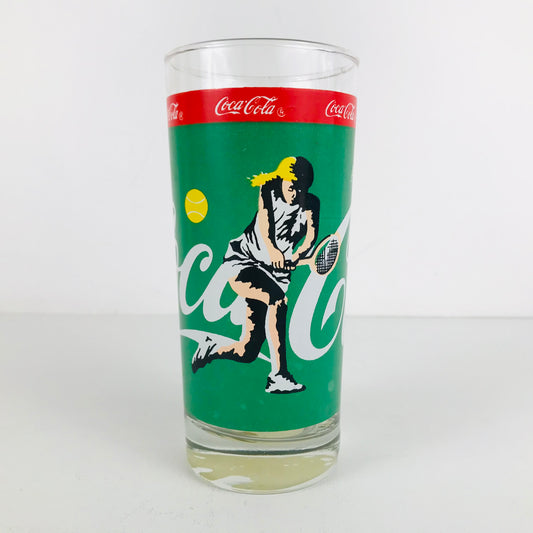 A vintage 1980s Coca Cola glass with a female tennis player swinging her racquet on the front.