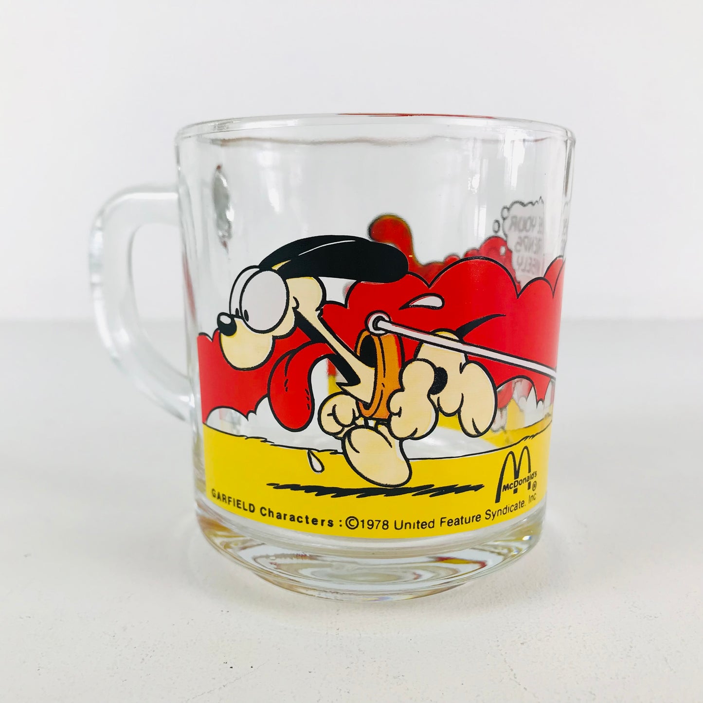 A 1980s McDonald's Garfield glass mug with a funny image of Odie tugging Garfield on a skateboard