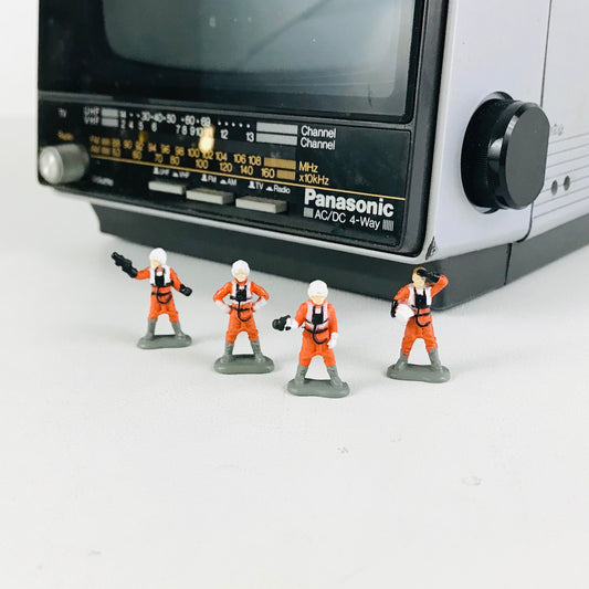 Four miniature Star Wars X-Wing Pilot figurines posed in front of a 1980s portable television