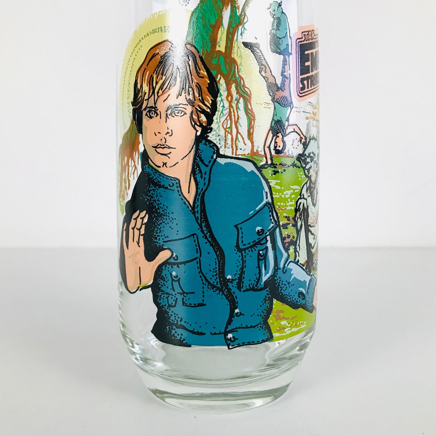 Close up shot of a 1980 Star Wars Empire Strikes Back glass tumbler featuring an image of Luke Skywalker in his Dagobah fatigues attempting to use the Force while holding his lightsaber.