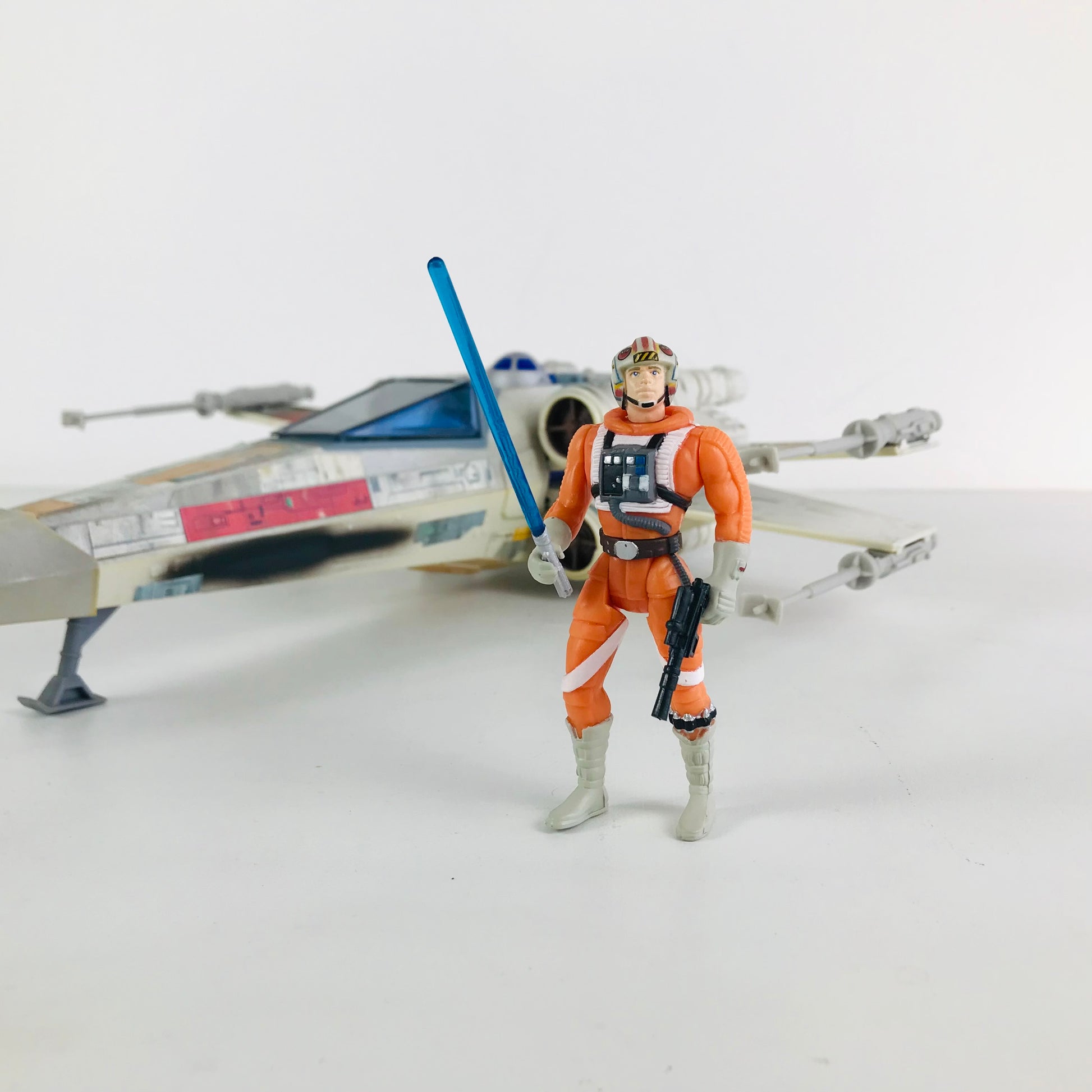 Luke Skywalker X-Wing Pilot action figure posed in front of his X-Wing Fighter vehicle while holding a blue lightsaber and blaster.