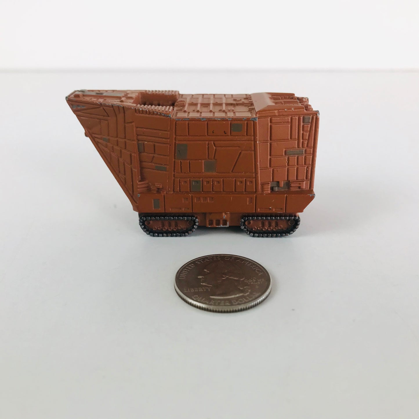 A miniature Star Wars Sandcrawler vehicle posed beside a quarter to show its scale