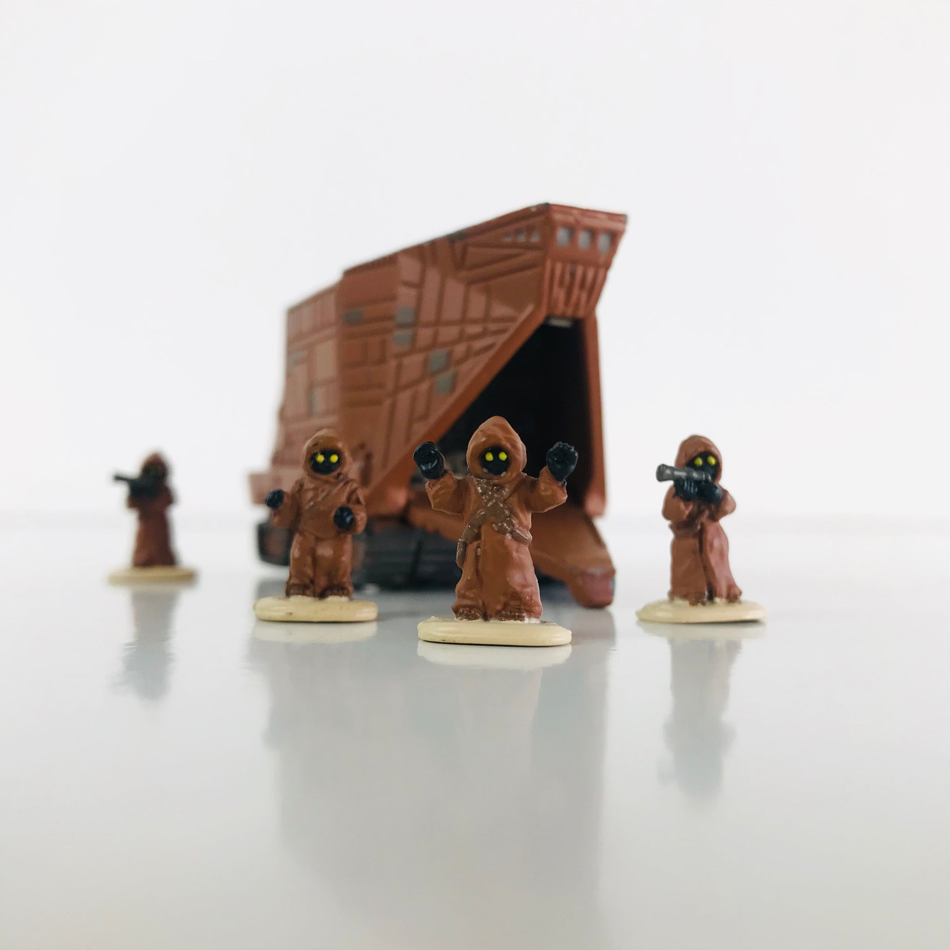 Four miniature Jawa figurines posed in front of their Sandcrawler vehicle