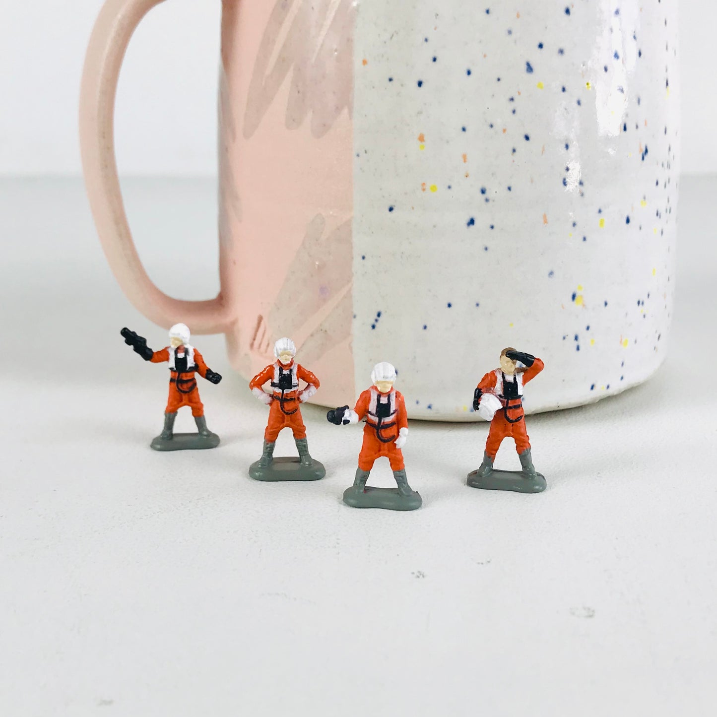 X-Wing Pilot figurines in various poses displayed in front of a speckled coffee mug